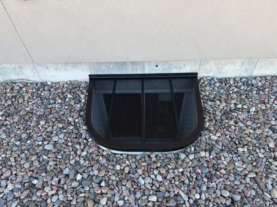 Black custom window well cover installed over rock landscaping