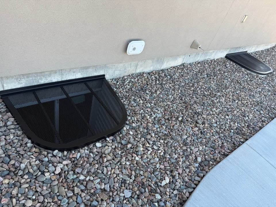 Multiple black custom window well covers installed along a foundation
