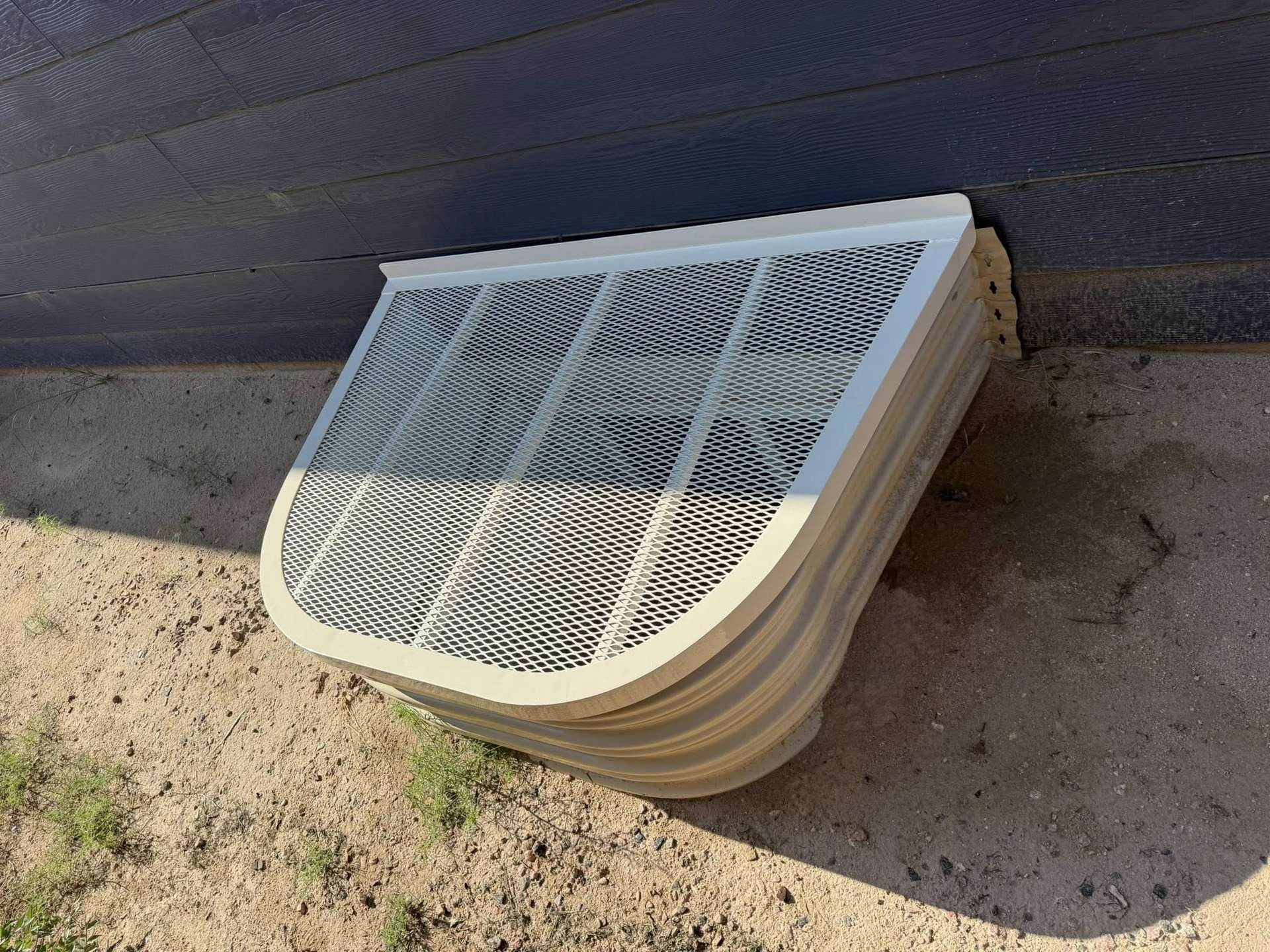 Light-colored custom window well cover installed against dark siding